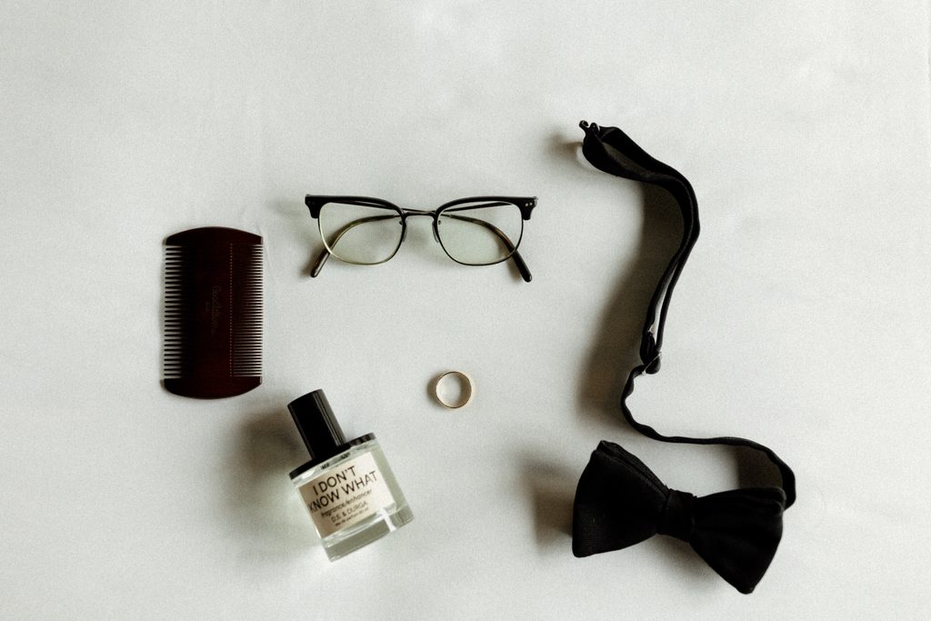 
Flat lay of groom Ryan’s wedding details, including his tie, glasses, cologne, and accessories, photographed at Bottleworks Hotel in Indianapolis, Indiana.