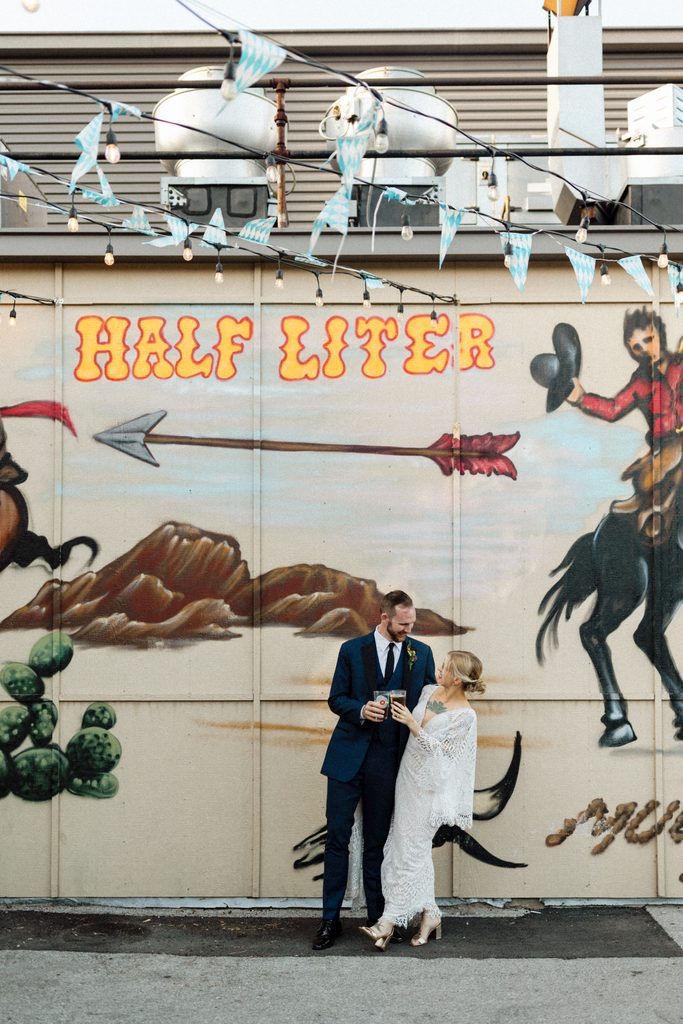 Kimmy and Ben walking together in front of a colorful mural at Liter House during their Indianapolis wedding.